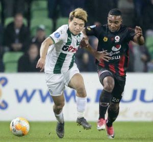 FCフローニンゲンのユニフォーム（白と緑）を着て、相手選手と激しく競り合いながらドリブル突破を図る堂安律