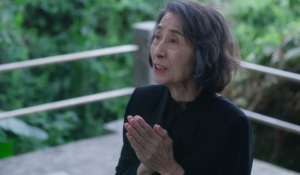 緑の背景を背に、黒い服装で手を合わせて話す香川京子さん