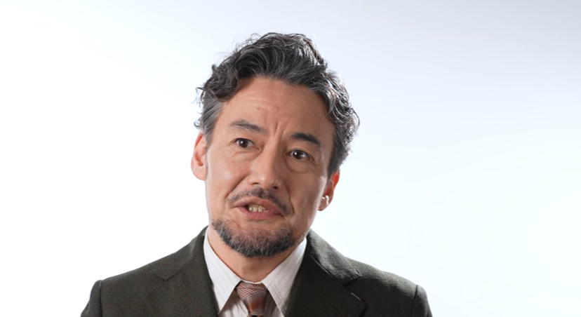 映画『侍タイムスリッパー』の主演、高坂新左衛門役を演じる俳優・山口馬木也のバストアップ写真。穏やかで誠実な表情を浮かべており、短髪で整えられた髭を蓄え、スーツを着用している。