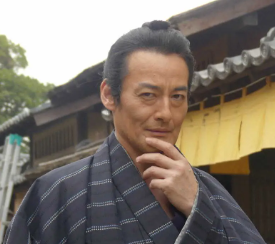 着物姿の侍(山口馬木也)が、片手を顎に添えて思案にふける表情を見せている。