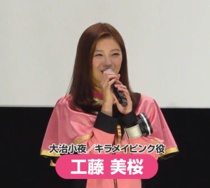 『魔進戦隊キラメイジャー』のイベントにて、マイクを手に微笑む工藤美桜。ピンクを基調とした華やかな衣装を纏い、ヒーローとしての自覚と、ファンへの感謝が滲む柔らかな表情。