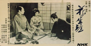 「1963年放送のNHK大河ドラマ第1作『花の生涯』のモノクロ場面写真。出演者の尾上松緑（井伊直弼役）、佐久間良子（村山たか役）、長野主膳役らが和室で対峙するシーン。」