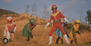 1975年、爆煙が立ち込める荒野に立つ、初代アカレンジャー（誠直也）を中心としたゴレンジャーの5人。スタントに頼らず、生身のアクションで「ヒーローの品格」をゼロから築き上げた、伝説の幕開けを象徴する一枚。