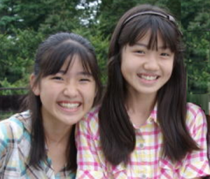 幼少期の村山彩希さん（右）と村山栞宇さんが、屋外で身を寄せて笑顔で写っている写真