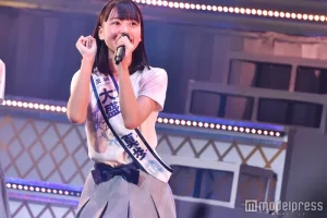 AKB48のステージ上で、「茨城」「大盛真歩」と書かれたタスキを肩にかけ、マイクを手に全力で歌い踊る大盛真歩。ドラフト3期生として加入し、選抜メンバーとして輝く彼女の情熱が伝わるライブパフォーマンス。