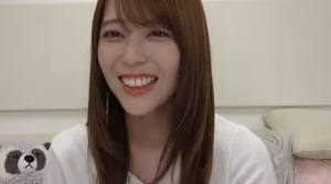 ライブ配信や動画番組での岩本蓮加。大人っぽく成長したロングヘア姿で、リラックスした表情で満面の笑みを浮かべている。背景にはぬいぐるみが置かれた室内。