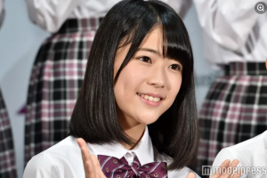 乃木坂46加入直後、中学1年生当時の岩本蓮加。白いシャツに紫のチェック柄リボンを着用し、初々しい笑顔でポーズをとるオーディション合格発表時の記者会見カット。