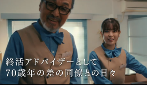 映画『世の中にたえて桜のなかりせば』の劇中カット。終活アドバイザーの制服を着て笑顔を見せる岩本蓮加と、ベテラン俳優の宝田明。画面には「終活アドバイザーとして70歳年の差の同僚との日々」というテロップが入っている。