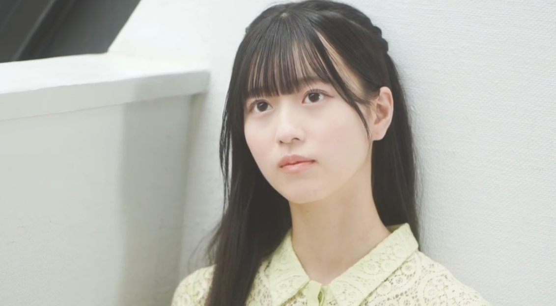 壁に背を預け、真っ直ぐな瞳で遠くを見つめるAKB48 18期生・八木愛月の表情アップ。黄色いレース柄の服を着用。