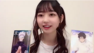 自宅のような場所で、大好きなアニメ『呪術廻戦』のキャラクター（五条悟と乙骨憂太）のイラストパネルを両手に持ち、満面の笑みで語る大盛真歩。アニメオタクとしての素顔が垣間見える一枚。