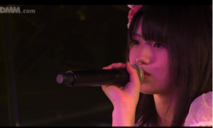 ピンク色のステージ照明の中、マイクを握りしめ、真剣なまなざしを見せる若い頃の村山彩希さんの写真