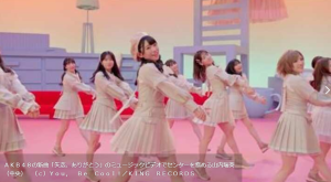 AKB48の57thシングル『失恋、ありがとう』のミュージックビデオで、淡いベージュの衣装を纏い中央で笑顔を見せるセンターの山内瑞葵と、左右で踊るメンバーたちのダンスシーン。背景にはパステルカラーの大きな椅子や家具が配置されている。