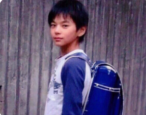 青いランドセルを背負い、少しはにかみながら振り返る小学生時代の佐藤勝利。現在の面影を強く残す幼少期の写真。