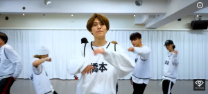 ダンス練習中の動画のクローズアップ。茶髪の橋本将生が中央に立ち、「橋本」と大きく漢字で書かれた白いビブスを着用している。彼の周りには他のダンサーが練習しており、画面右下には「VOYZ BOY」のロゴが表示されている。