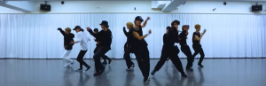広いスタジオで約10人の「VOYZ BOY」のメンバーが白いカーテンの前でダンスの振り付けを練習している。彼らは黒や白の様々な練習着を着ており、躍動感のあるポーズをとっている