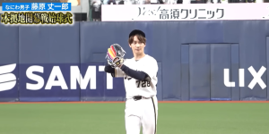 野球場での始球式。なにわ男子の藤原丈一郎が、背番号728のユニフォームとカラフルなグローブを着用し、投球ポーズをとっている。