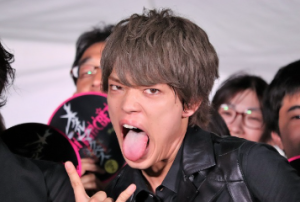 イベント会場でファンを背に、舌を出して手でロックポーズを決めるお茶目でワイルドな表情の原嘉孝