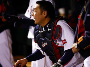 野球日本代表（侍ジャパン）のユニフォームとキャッチャー防具を身につけ、ベンチから真剣な眼差しで戦況を見つめる阿部慎之助選手