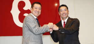 読売ジャイアンツの球団旗を背に、笑顔でグータッチを交わす原辰徳氏とスーツ姿の阿部慎之助新監督