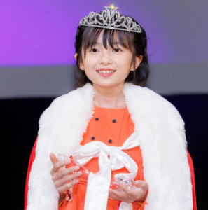 ティアラと赤いドレス、白いファーを身につけ、ガラスの靴を持って微笑む白山乃愛