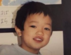 背後にひらがなで名前が書かれた作品が飾られている、あどけない笑顔を浮かべる幼少期の原嘉孝