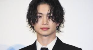 ウェット感のあるウェーブヘアに黒のスーツを身に纏い、落ち着いたクールな表情で正面を見据える綱啓永のショット